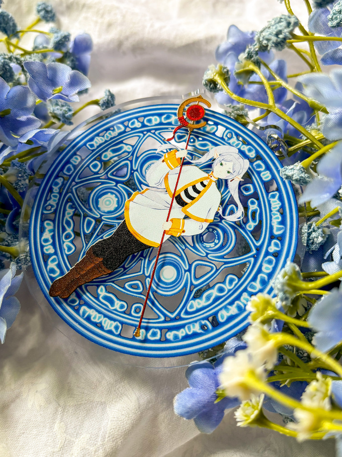 Acrylic charm featuring Frieren in a white and black outfit holding a red staff, with magic spell in the background.