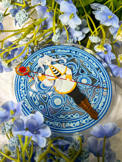 Acrylic charm featuring Frieren in a white and black outfit holding a red staff, with magic spell in the background.