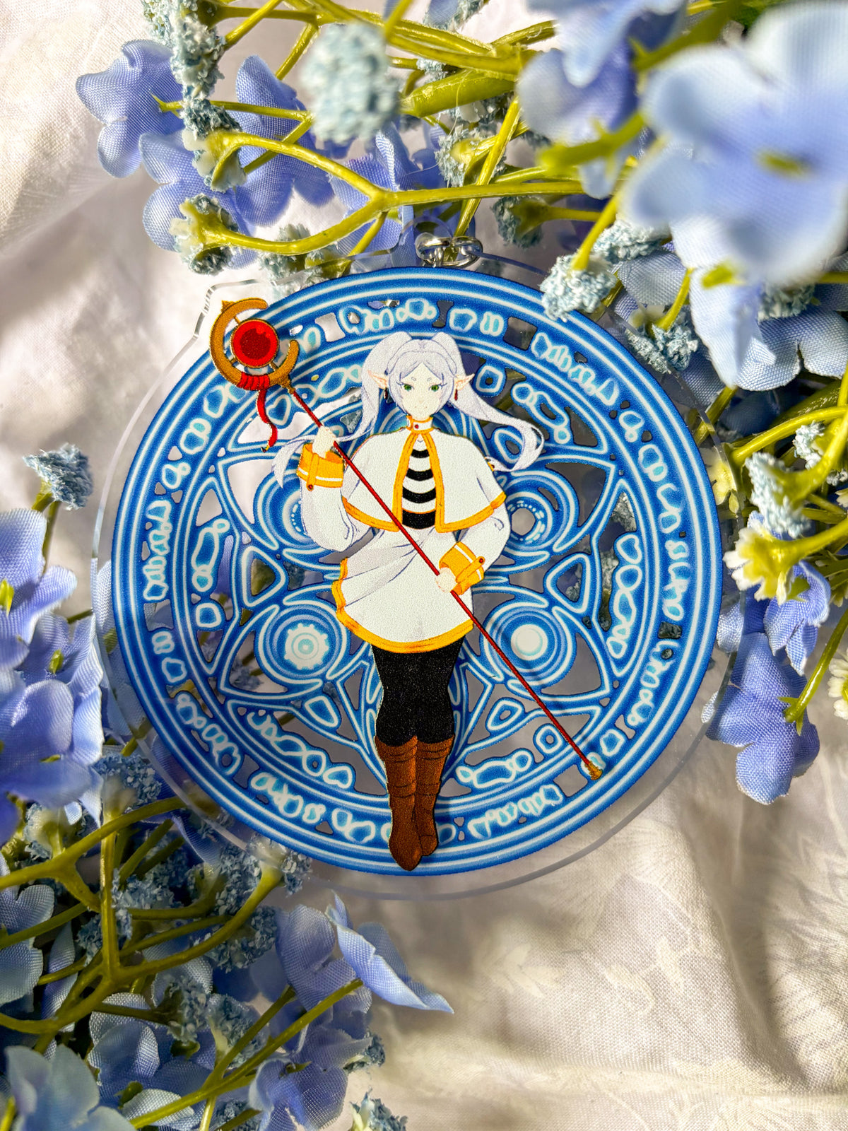 Acrylic charm featuring Frieren in a white and black outfit holding a red staff, with magic spell in the background.