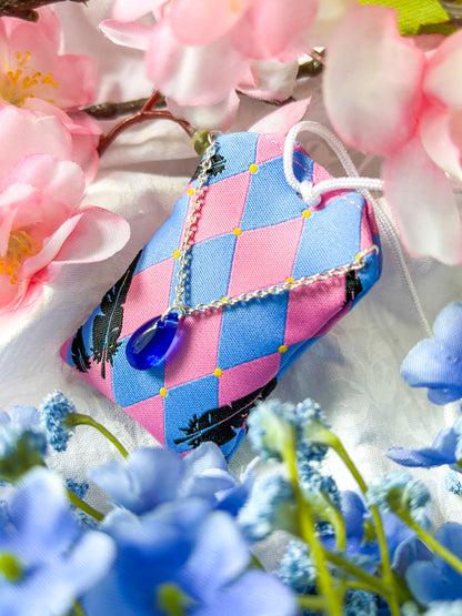 Japanese good luck charm (omamori) based on the Studio Ghibli movie Howl's Moving Castle. This is a pink and blue fabric charm that displays Howl's black feathers and Howl's blue stone necklace.