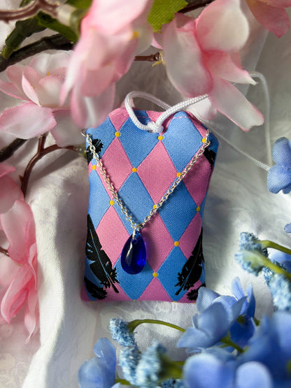 Japanese good luck charm (omamori) based on the Studio Ghibli movie Howl's Moving Castle. This is a pink and blue fabric charm that displays Howl's black feathers and Howl's blue stone necklace.