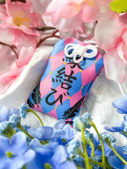 Japanese good luck charm (omamori) based on the Studio Ghibli movie Howl's Moving Castle. This is a pink and blue fabric charm that displays Howl's black feathers and Howl's blue stone necklace.