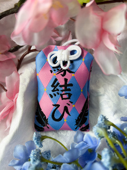 Japanese good luck charm (omamori) based on the Studio Ghibli movie Howl's Moving Castle. This is a pink and blue fabric charm that displays Howl's black feathers and Howl's blue stone necklace.
