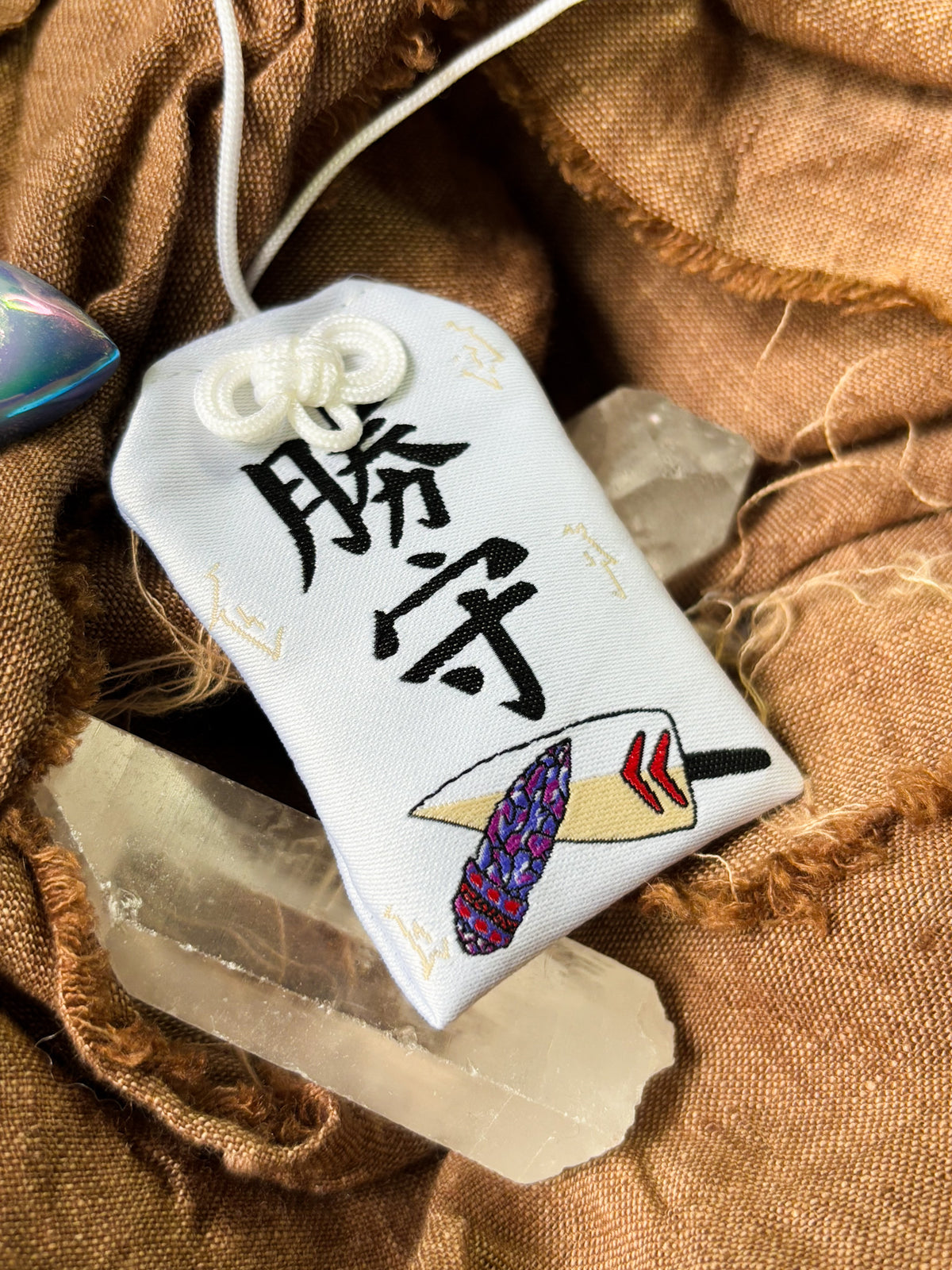 Japanese good luck charm (omamori) based on the Studio Ghibli movie Princess Mononoke. This is a mostly white fabric charm that displays San's dagger alongside the gem dagger gifted to San from Prince Ashitaka.