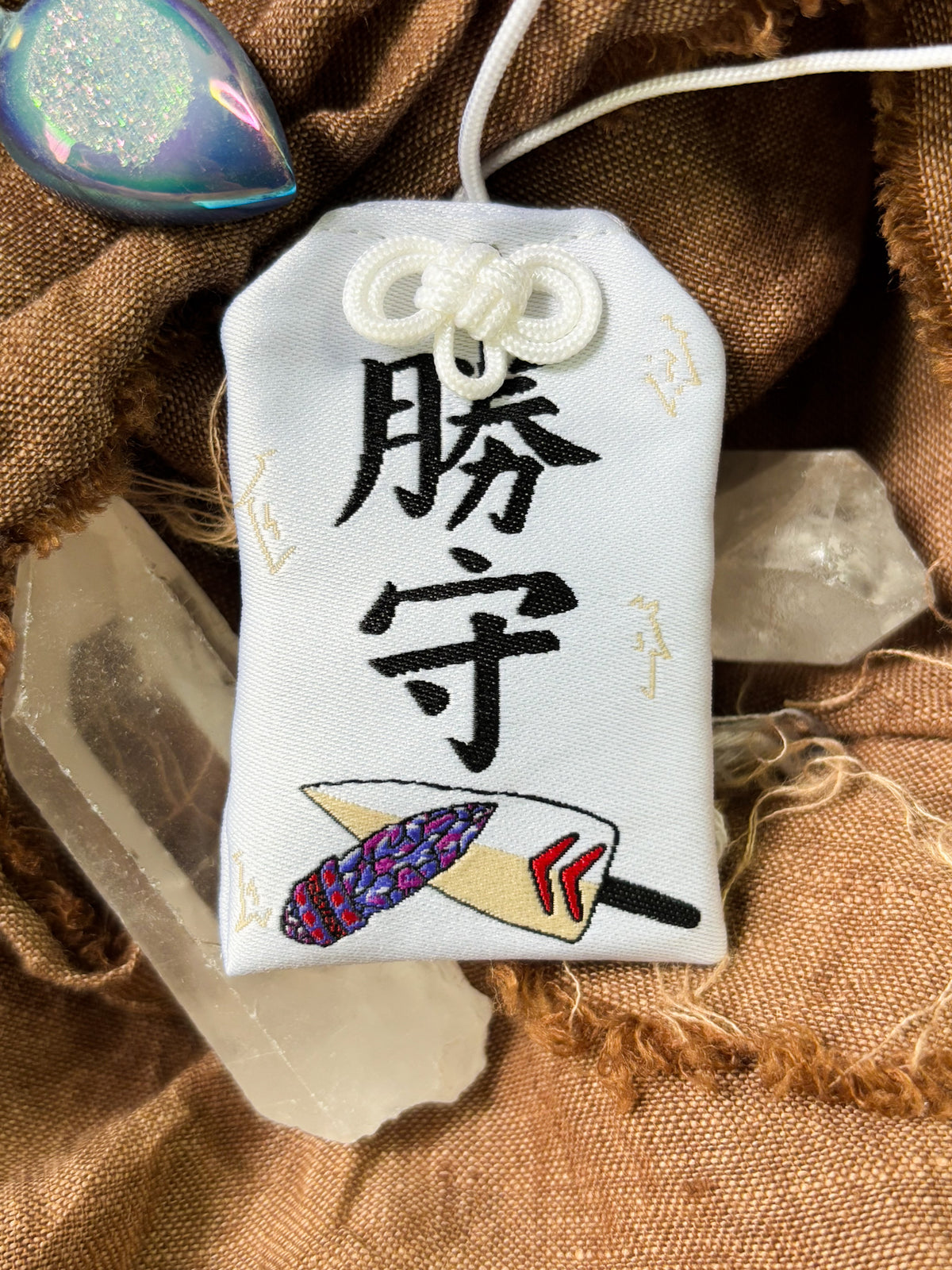 Japanese good luck charm (omamori) based on the Studio Ghibli movie Princess Mononoke. This is a mostly white fabric charm that displays San's dagger alongside the gem dagger gifted to San from Prince Ashitaka.