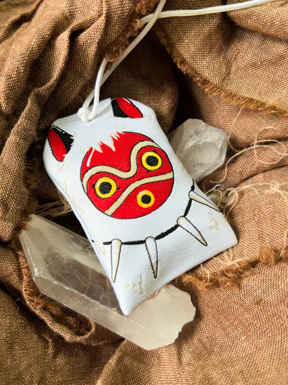 Japanese good luck charm (omamori) based on the Studio Ghibli movie Princess Mononoke. This is a mostly white fabric charm that displays San's mask and necklace. Charm replicates San's white fur cape. 