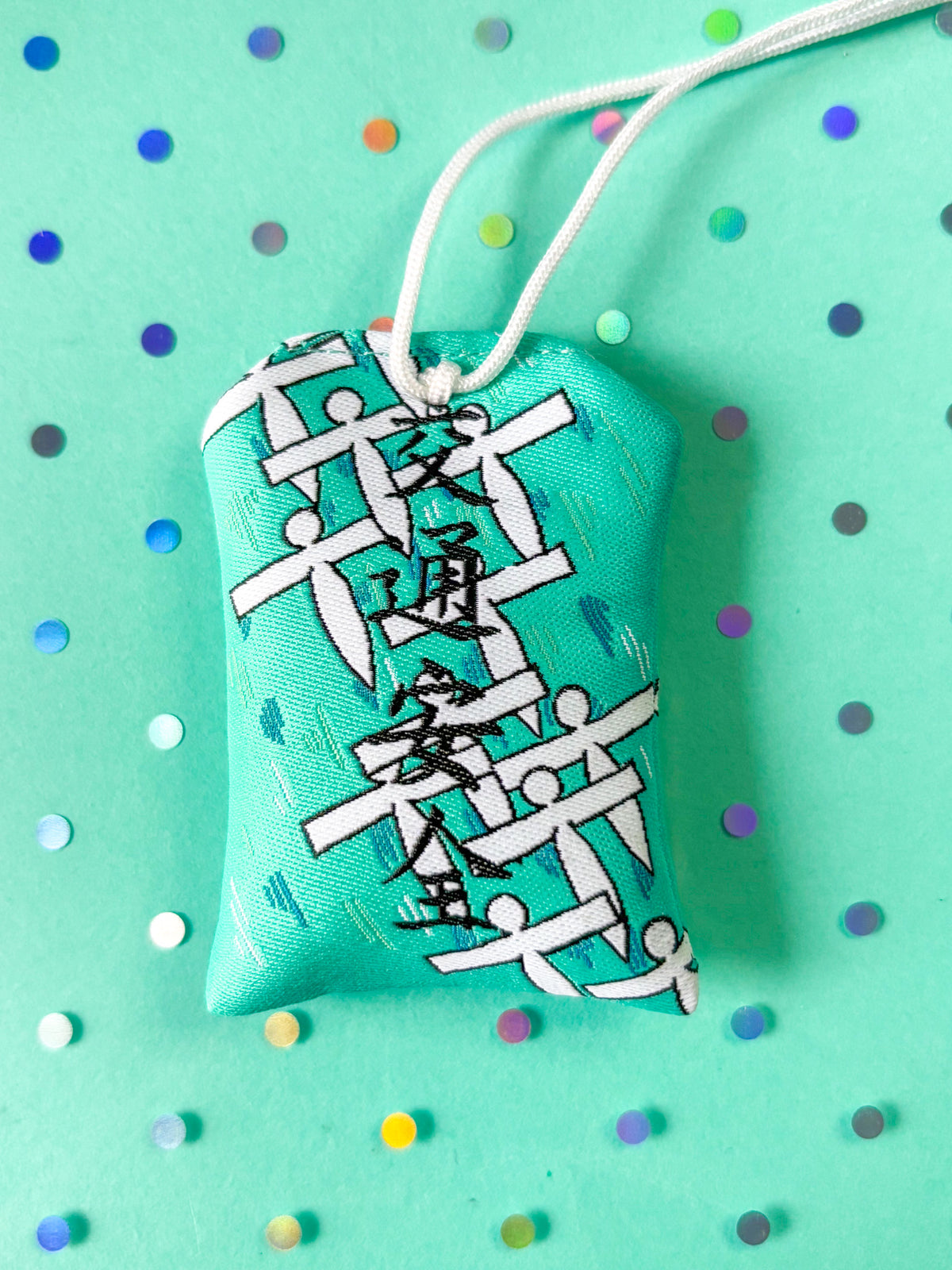 Japanese good luck charm (omamori) based on the Studio Ghibli movie Spirited Away. Based on the Paper Spirit characters. This is a teal (green-blue) fabric charm that displays the Paper Spirits flying over water.