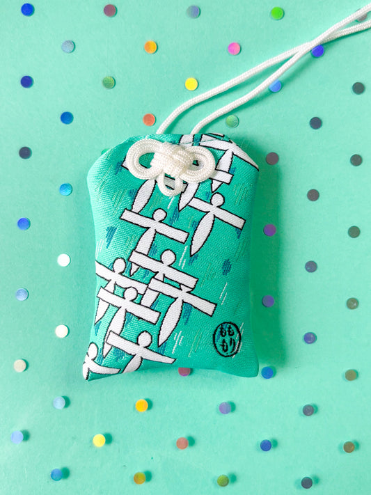 Japanese good luck charm (omamori) based on the Studio Ghibli movie Spirited Away. Based on the Paper Spirit characters. This is a teal (green-blue) fabric charm that displays the Paper Spirits flying over water.