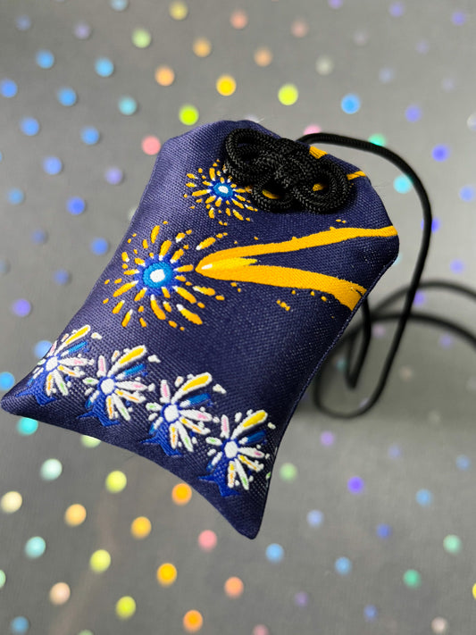 Japanese good luck charm (omamori) based on the Studio Ghibli movie Howl's Moving Castle. Based on the Star Children characters. Charm shows colorful firework-like designs with the Star Children lining the bottom.